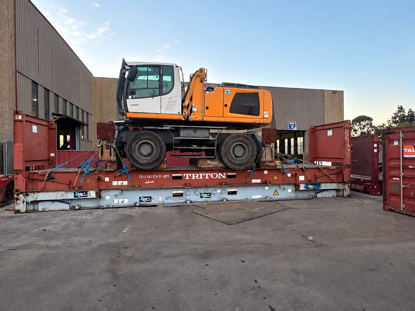 Used wheeled excavator secured on a flat rack container